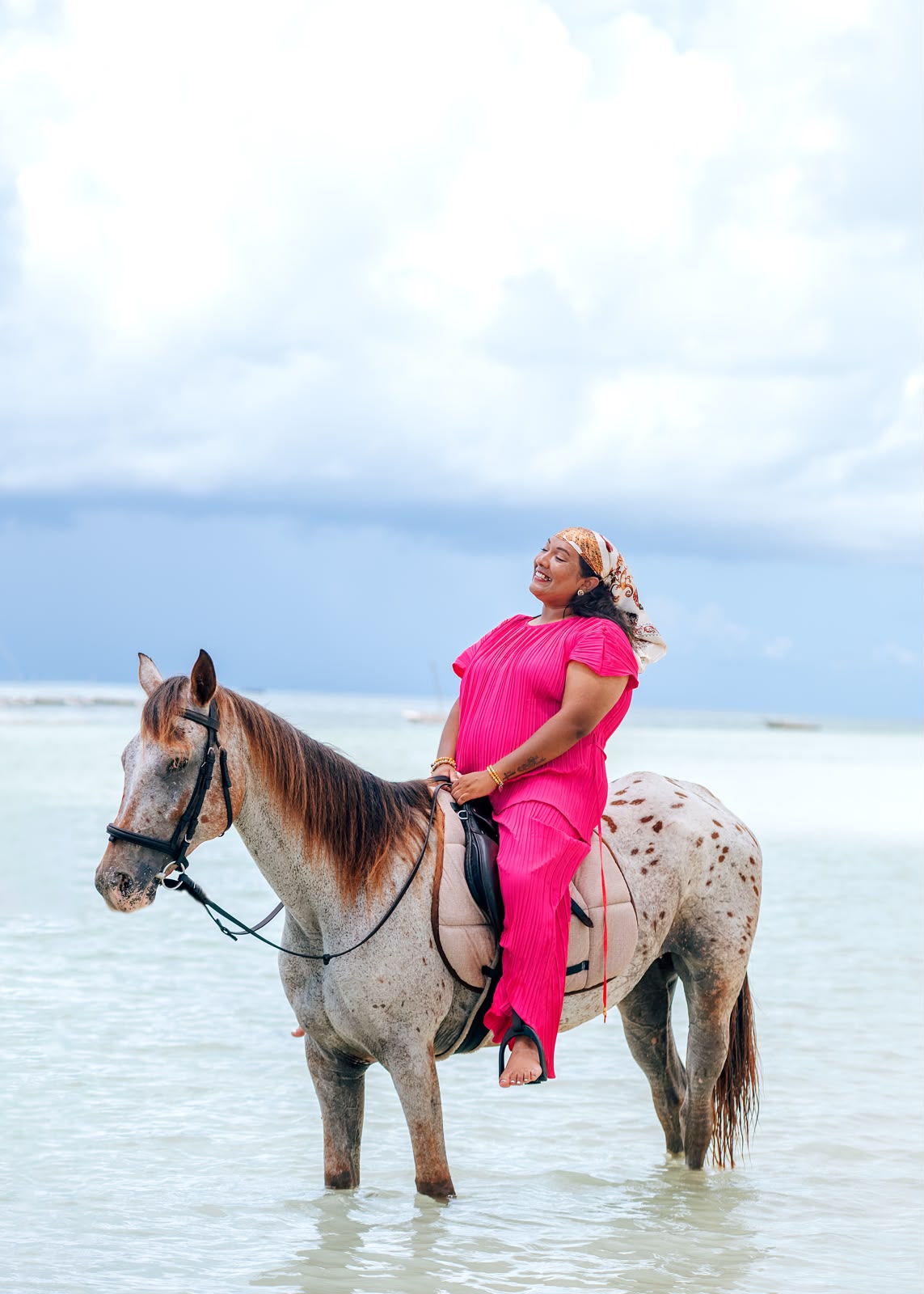 Beach horse riding in Paje, Zanzibar — guest in a bright pink dress laughing on a spotted horse in the water
