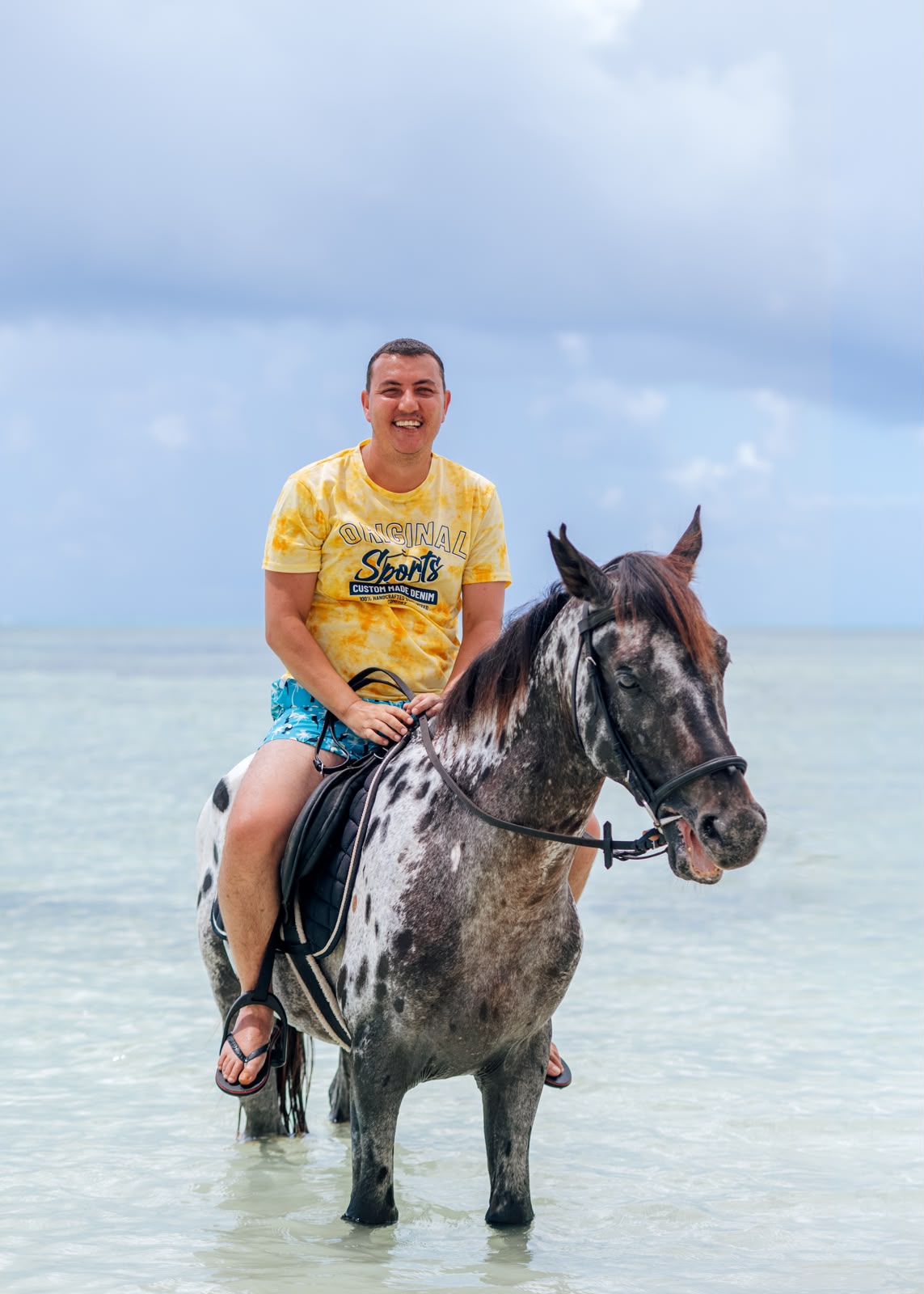 Beach horse riding in Paje, Zanzibar — guest smiling on a spotted horse standing in clear shallow water