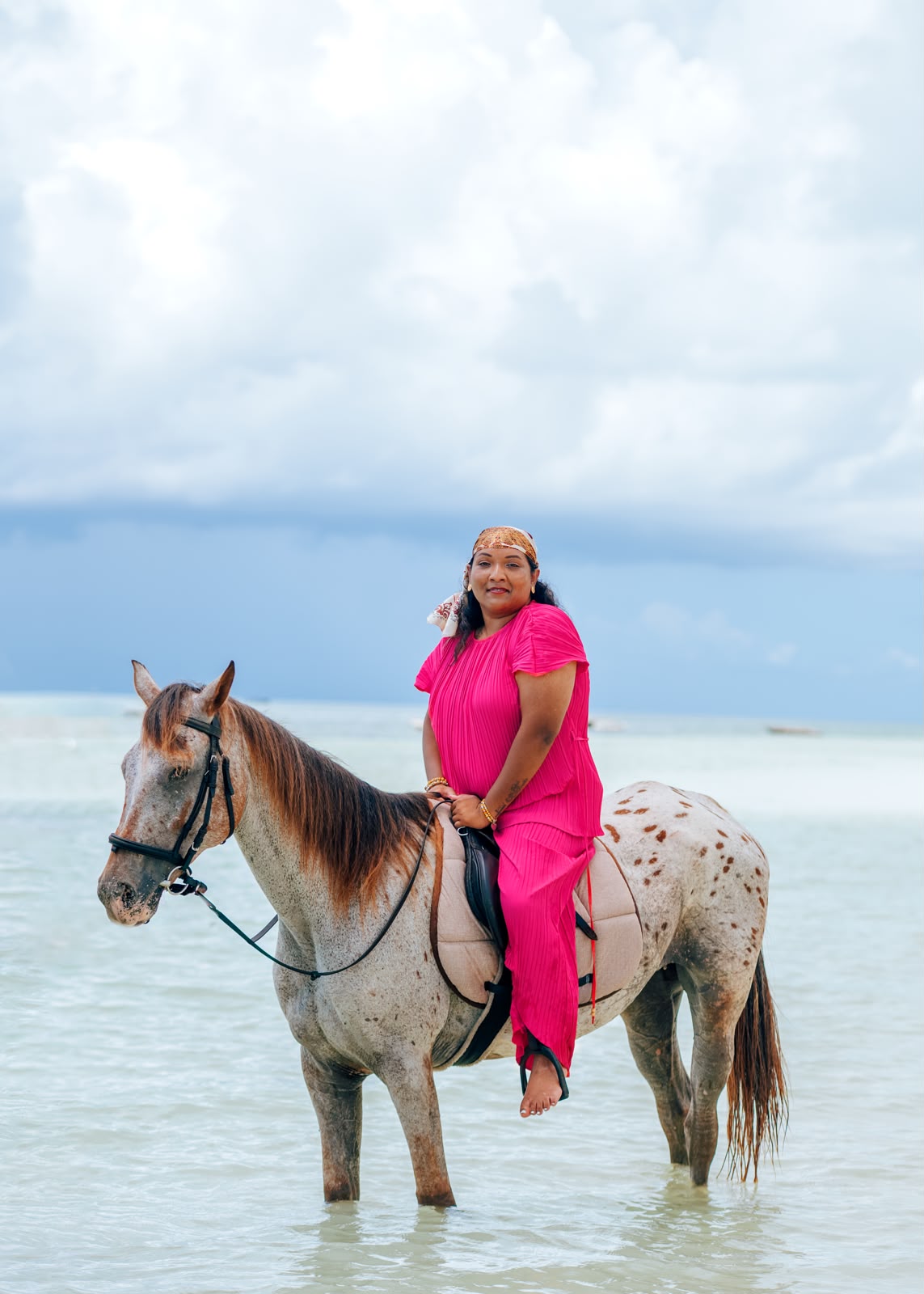 Beach horse riding in Paje, Zanzibar — guest in pink posing on a spotted horse under a cloudy sky